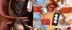 Two monks reading scripture while seated at a table laid out with pastries, watermelon and bananas