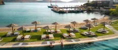Sandy beach and lawn with loungers and parasols sandwiched between a swimming pool and the sea