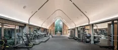 Triangular-roofed gym with large mirrors one side and large windows the other, lined with treadmills, two rowers, weight machines and exercise balls,