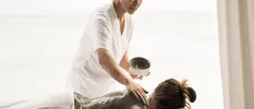 Therapist applies mud to a woman's back as she lies on her front on a massage mus