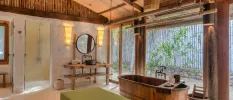 Villa bathroom with a wooden ceiling, vanity unit and bathtub, bohemian lighting and full-length windows overlooking leafy shrubs