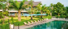 Rectangular pool in a tropical garden, with rattan loungers and blue umbrellas at the water's edge