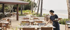 Woman sets tables an a beachfront terrace with the ocean in the background