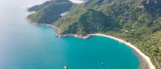 Aerial view of green hillsides, with a slice of white sand at the bottom and turquoise sea lapping the beach