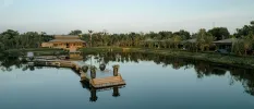 Wooden building with a grey-tiled roof, overlooking a river and wooden jetty and surrounded by greenery
