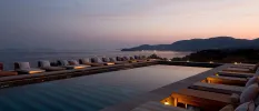 Twilight by a sea-facing pool, with chic striped daybeds, in-wall lighting and a view of the mountains in the background