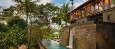 Infinity pool with a waterfall, which flows down a stone wall underneath a building with full-length windows