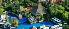 Lagoon-like swimming pool surrounded by greenery, thatched triangular rooftops and red-walled buildings