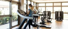 Woman in Nike trainers and a grey t shirt running on a treadmill in a bright gym with full-length windows