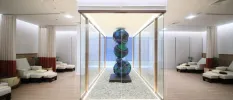 Glass case with a contemporary sculpture shaped like three stacked balls, surrounded by white-cushioned daybeds