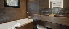Brown marble bathroom with mosaic tiles, a large mirror and vanity unit and white bath