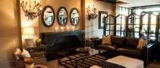 Cosy seating area with a brown leather sofa, dark-wood and glass coffee table, biscuit-coloured walls, and chandeliers styled like vines