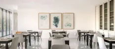 Airy restaurant with white walls and glossy floors, grey and black tables and chairs and framed monochrome pictures on the wall