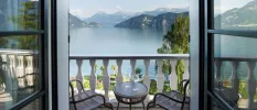 Balcony with white balustrades, a table and chairs and a view of a lake framed by mountains