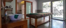 Treatment room with massage bed and white sink with a large window overlooking tropical greenery