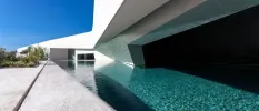Wedge-shaped swimming pool next to an angular white building with a large dark window