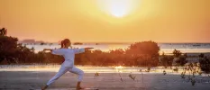 Woman in white practices yoga on the beach as the sun rises or sets