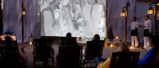 Black and white movie showing on a large screen with an audience seated in deck chairs