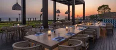 Outdoor restaurant terrace with a bohemian feel, with rattan pendant lights and furniture, and a view of the sea at sunset