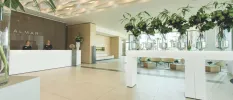 Smiling receptionists in a marble lobby with multiple vases of flowers, and a sign that reads 'Almar Jesolo Resort & Spa'