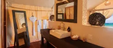 Bathroom with dark-wood mirrors and vanity unit, with a white butler sink and black rattan lanterns and a white robe hanging in the corner