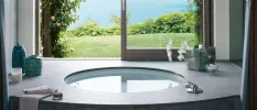 Vanity unit with a round sink and accessories under an open window with a garden and lake view