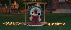 Lady sitting on a grass surrounded by candles and playing a large gong