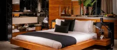 Low-rise wooden bed with crisp white bedding and navy pillows and a navy throw, overlooked by wooden Buddha statues, flowers and a fruit platter