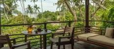 Wooden balcony with a sofa, tables and chairs overlooking tropical gardens and the beach