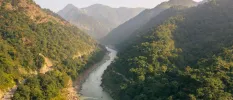 A curvy river runs along green-cloaked peaks under a misty blue sky
