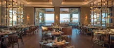 Modern softly lit restaurant with simple wooden furniture and full-length windows with a sea view