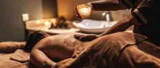 Woman lying down in a softly lit room receiving a massage with candles in the background