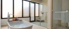 Bathroom with a large standalone tub with running water, a walk-in shower with glass doors and frosted windows