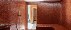 Wellness room covered in mosaic-style pink tiles, with a bench and shower head