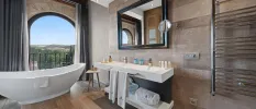Bathroom with tiled walls and a wooden floor, a standalone bathtub and a view of the countryside from an arched window