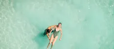 Woman in a grey swimsuit with her eyes closed floats on her back in water supported by a team member