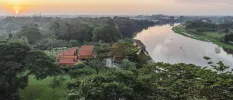 Terracotta-tiled rooftops peering out from tropical greenery next to a river at sunset