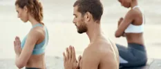 Three people in active wear sitting in lotus position with their hands in prayer position