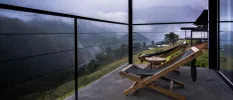 Balcony with dark deck chairs overlooking misty mountains and forested slopes