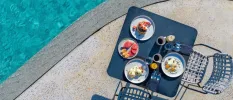 Poolside table set for breakfast, with plates of watermelon, fried and poached eggs, and a pancake stack topped with blueberries and strawberries