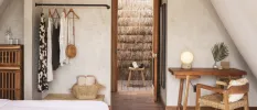 Room with white walls and flooring, a wooden desk area, wardrobe space with black and white clothes and rattan handbags, and an outdoor shower showing through a doorway