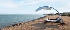 Wooden loungers with squidgy white cushions and a curved parasol over the top on the sandy shoreline