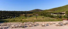 Sandy beach lined with daybeds and loungers, with a backdrop of pine forests and rolling hills