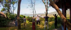 Group in loose fitting clothes enjoy a class in a garden with an ocean view