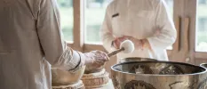 Two people in white loose fitting clothes stand over sound bowls