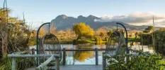 A lake framed by greenery and mountains, with a wooden deck and egg-shaped wicker chairs for enjoying the view