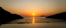 Infinity-edge pool with a view of the sea and surrounding hillsides and the sun setting over the horizon