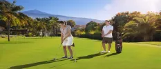 Man and woman enjoy golf under a sunny sky with Mount Teide in the background 