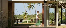 Man in traditional dress walking through an open-air furnished terrace overlooking tropical palm trees and greenery