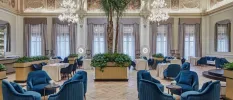 High-ceiling room with chandeliers, a central palm tree and tables with white clothes and blue velvet chairs